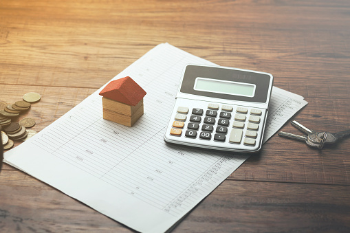 A small house figurine sitting on top of paperwork next to a calculator