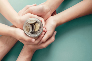 Three sets of hands holding a jar of change
